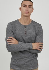 Grå langermet henley-skjorte med knappestolpe, laget av teksturert stoff. Har enkle sømmer og et lite logomerke i kanten.