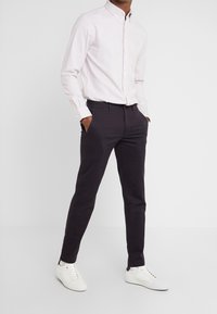 Jasnoróżowa koszula zapinana na guziki z długimi rękawami, zestawiona z ciemnofioletowymi chinosami i białymi trampkami. Casualowy fason o eleganckim kroju.