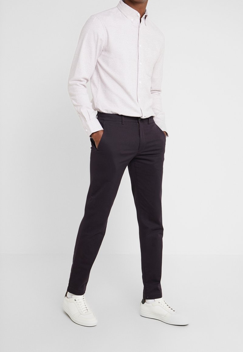 Jasnoróżowa koszula zapinana na guziki z długimi rękawami, zestawiona z ciemnofioletowymi chinosami i białymi trampkami. Casualowy fason o eleganckim kroju.