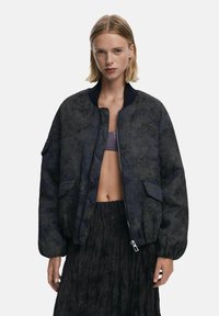 Textured bomber jacket in dark blue with a floral pattern, ribbed collar, and front pockets. Features a zip closure and relaxed fit.