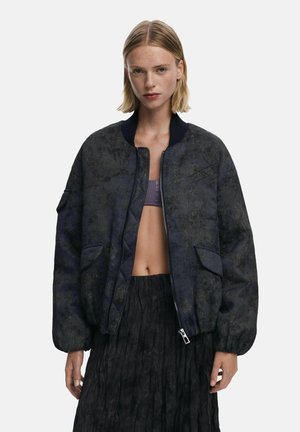 Textured bomber jacket in dark blue with a floral pattern, ribbed collar, and front pockets. Features a zip closure and relaxed fit.
