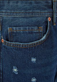 Temno modri jeans iz denima z bledim vzorcem, ki vključujejo več manjših uničenih predelov in dodaten žep z oranžnim šivom.