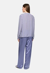 Leichte Bluse mit einem blau-weißem geometrischen Muster, kombiniert mit glänzenden, locker sitzenden hellblauen Hosen. Glatte Stofftextur.