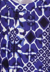 Niebiesko-biała tkanina w wzór z geometrycznym motywem, zawierająca kształty jak diamenty i kwiaty, o miękkiej fakturze i marszczeniach.