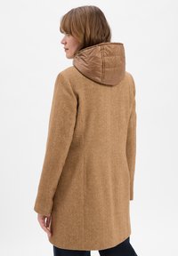 Brauner Herringbone-Mantel mit einer wattierten, hellbraunen Kapuze, tailliertem Schnitt und glatter Textur. Die Rückseite ist schlicht mit dezenten Nahtdetails.