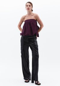 Strapless bordeaux top met gather-detail, gecombineerd met glanzende zwarte wijde broek met cargozakken en chunky haksandalen.