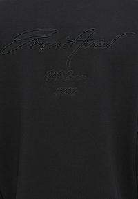 Zwarte sweatshirt met textuur van zwart borduurwerk van "Giorgio Armani Milano 1981" op de rug, met een zachte, gladde stoftextuur.