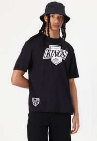 Svart t-skjorte med kort erme som har et hvitt grafisk design med teksten "Los Angeles Kings" på forsiden, samt en liten logo på sømmen.