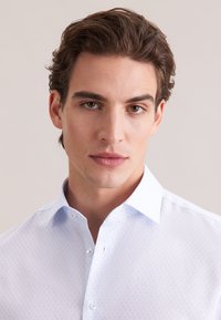 Lichtblauw overhemd met knopen, voorzien van een subtiel diamantpatroon, spitse kraag en enkele knoopsluiting bij de hals. Zachte stoftextuur.