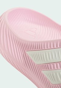 Gros plan sur une sandale slide rose texturée avec des rayures diagonales blanches en relief sur le côté et une semelle intérieure profilée.