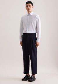 Witte overhemden met marineblauwe stippen, gecombineerd met op maat gemaakte marineblauwe broek en zwarte veterschoenen. Gladde stof, klassieke pasvorm.