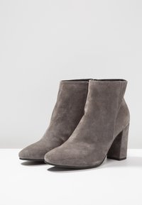 Bottines en daim gris avec un bout pointu et un talon épais. Texture lisse et design minimaliste, dotées d'une fermeture éclair latérale.