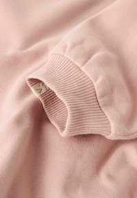 Tessuto rosa morbido con un dettaglio a polsino rigato, che mostra texture e pieghe delicate, evidenziando la manica di un indumento accogliente.