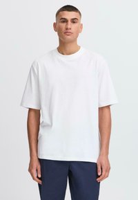 Hvid bomulds t-shirt med en afslappet pasform, korte ærmer og rund halsudskæring. Kombineret med marineblå bukser, der har en glat tekstur.