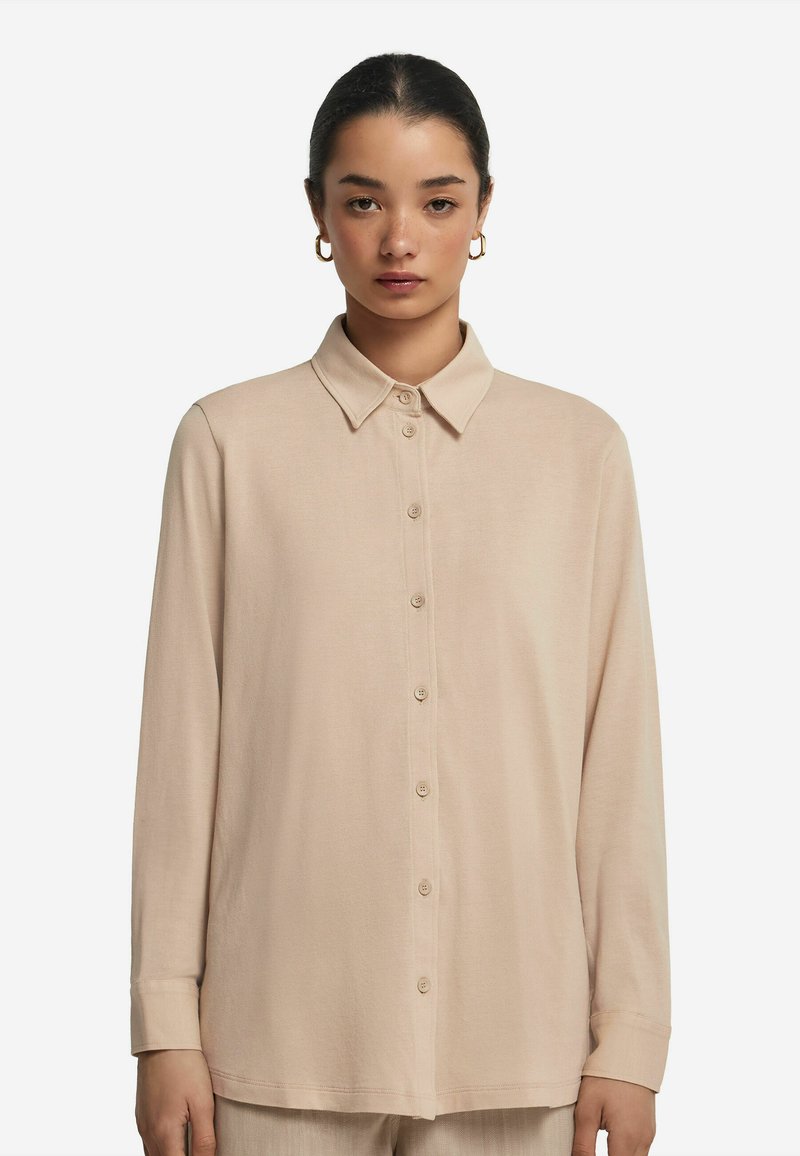 Långärmad skjorta i ljus beige, gjord av mjukt tyg. Har en klassisk krage och en knappslå framtill med sex knappar.