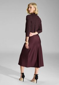 Suéter corto burdeos con brillo, mangas 3/4, combinado con una falda burdeos elegante hasta el suelo. Zapatos de tacón alto en negro y nude.