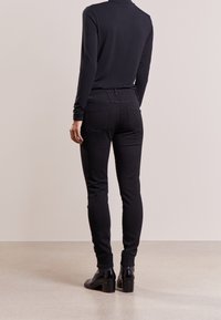 Jeans elasticizzati neri con una vestibilità slim, caratterizzati da una vita media, tasche posteriori e una texture liscia. Abbinati a stivaletti neri.