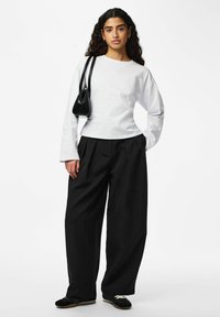 Chemise blanche à manches longues, pantalon noir taille haute à jambes larges, et chaussures noires. Petit sac noir avec bandoulière.