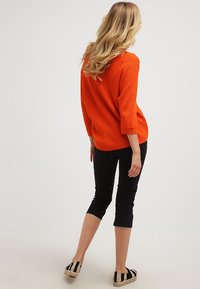 Oranges geripptes Sweatshirt mit Dreiviertelärmeln, kombiniert mit schwarzen Caprihosen und schwarz-weißen gestreiften Espadrilles.