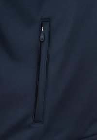 Tessuto blu navy con una superficie liscia, caratterizzato da una tasca con zip verticale al centro e cuciture rinforzate lungo i bordi.