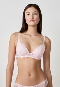 Różowy koronkowy biustonosz o trójkątnym kształcie, z falbaniastymi krawędziami i małą kokardką na środku. Ramiączka są cienkie i regulowane, z teksturowanymi wzorami.