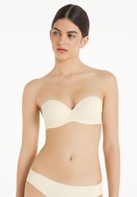 Helle beige trägerlose BH mit glatten, geformten Körbchen, Stütze durch Bügel und minimalistischen Design. Weicher Stoff mit nahtlosen Kanten.