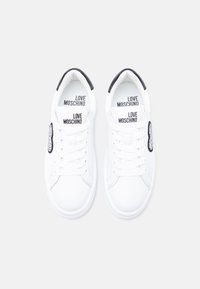 Ζευγάρι λευκά αθλητικά παπούτσια Love Moschino με μαύρες λεπτομέρειες στη φτέρνα και κορδόνια μπροστά, σε άποψη από πάνω σε λευκό φόντο.