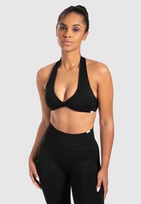Zwarte haltertop met een gedraaid voorontwerp, gecombineerd met hoge zwarte leggings. Soepele stof met een matte afwerking.
