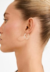 Silver hoop earring displayed on a model’s ear, featuring a smooth, circular design with a slightly textured surface.