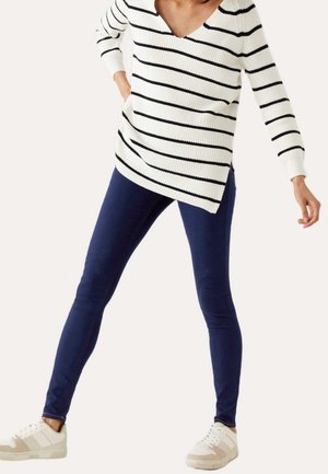 Suéter blanco con rayas negras y escote en V, combinado con unos jeans ajustados de color azul oscuro y zapatillas blancas con acentos beige.