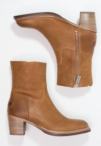 Botas de tobillo de cuero marrón con un acabado texturizado, una cremallera lateral y un tacón apilado. El diseño presenta una punta redondeada y bordes suaves.