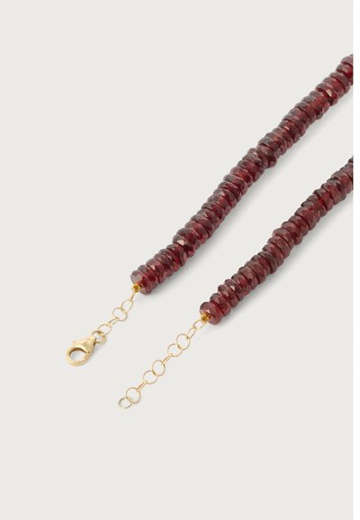 Piros, facettált gyöngyök egy fonaton, arany zárral és lánc alkatrésszel. Simább textúra, fényes felülettel.