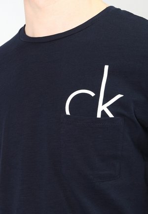 Námořnická modrá bavlněná tričko s kulatým výstřihem, se zlatým potiskem loga na levé kapsičce. Měkká textura, ležérní design.