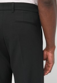 Schwarze Hosen aus gewebtem Stoff mit glatter Textur, ausgestattet mit einer einzelnen Gesäßtasche und einer maßgeschneiderten Passform.