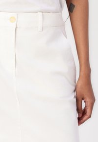 Jupe en coton blanc avec une fermeture à boutons à l'avant, une taille avec passants de ceinture et des poches latérales. Texture fluide avec une coupe ajustée.