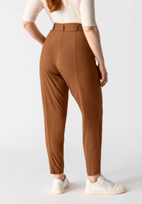 Pantalones marrones, ajustados y de talle alto, hechos de un tejido elástico; combinados con zapatillas blancas, mostrando una textura y un ajuste suaves.