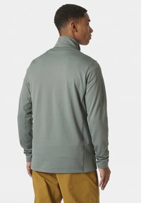 Suéter gris de manga larga con cuello alto, tejido texturizado y costuras planas, combinado con pantalones marrón claro.