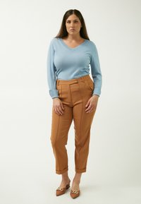 Lysblå langærmet trøje med V-hals, parret med brune skræddersyede bukser med forreste sømme. Brune mule-sko med dekorative detaljer.