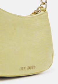 Sac à main texturé jaune clair avec fermeture éclair et bandoulière chaîne dorées, avec logo Steve Madden doré sur la partie avant inférieure.