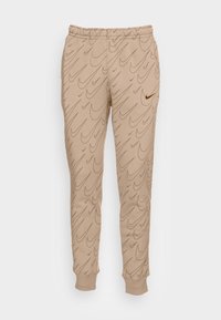 Pantalones jogger beiges hechos de una tela suave, con un patrón de swoosh repetido en un tono ligeramente más oscuro, cinturilla elástica y puños en los tobillos.