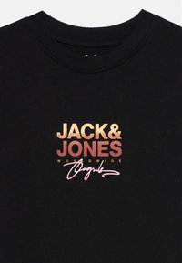 Black cotton T-shirt featuring a gradient text logo in gold and red, with "JACK & JONES" and "WORLDWIDE" above a pink signature.