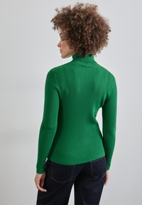 Pull à col roulé vert côtelé avec une coupe ajustée, des manches longues et un tissu texturé. Détails de couture visibles au niveau du col et de l'ourlet.