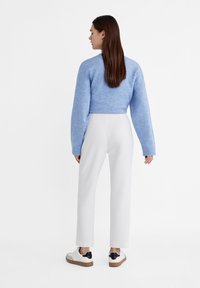 Lichtblauwe cropped trui met brede mouwen, gecombineerd met witte rechttoe-rechtaan broeken en witte sneakers met zwarte accenten.