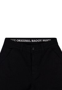 Černé široké kalhoty s knoflíkovým zapínáním a bočními kapsami. Elastický pás nese nápis "THE ORIGINAL BAGGY PANTS" v bílé barvě.
