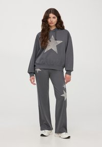 Szary zestaw z bawełnianą bluzą z kapturem i spodniami, ozdobiony dużymi srebrnymi gwiazdami, o luźnym kroju i kapturze ze sznurkiem, zestawiony z białymi trampkami.