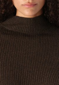 Pull en col roulé marron à côtes avec un col haut ; doté d'un tricot texturé, d'une coupe près du corps et de fibres naturelles pour la chaleur.