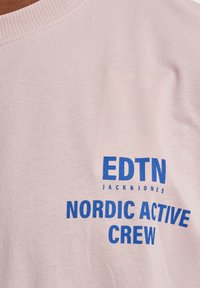 Lyserød bomulds t-shirt med rund hals og blå tekstprint: "EDTN JACK & JONES" over "NORDIC ACTIVE CREW." Glat tekstur.