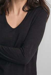 Haut noir à manches longues avec un décolleté en V. Tissu doux et texturé avec une silhouette ajustée, présentant des détails subtils de coutures le long des manches.