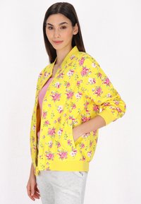Giacca bomber gialla floreale con motivi di rose rosa e bianche; polsini e orlo a coste; due tasche; tessuto leggero.