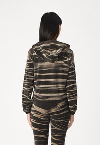 Hoodie u tamnosmeđoj boji s kremastim valovitim prugama, s elastičnim rukavima i rubom. Tkanina izgleda mekano s teksturiranim finišom.
